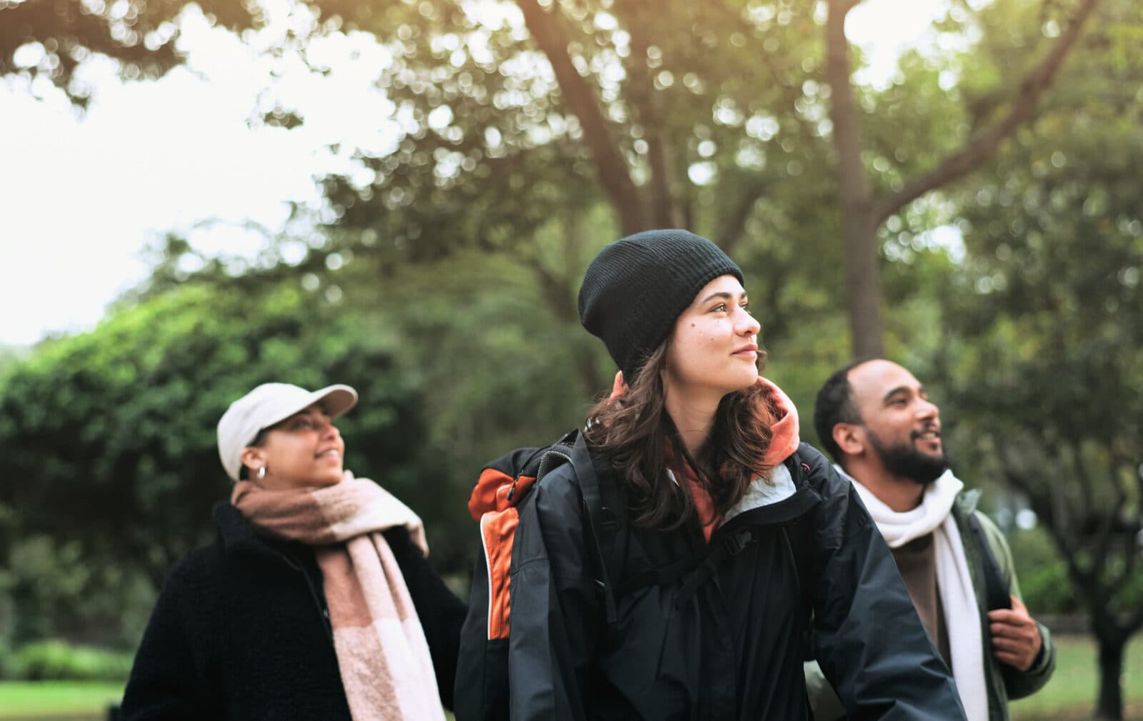 Bilden visar tre personer som promenerar utomhus i en park. De ser glada ut och är klädda i varma ...
