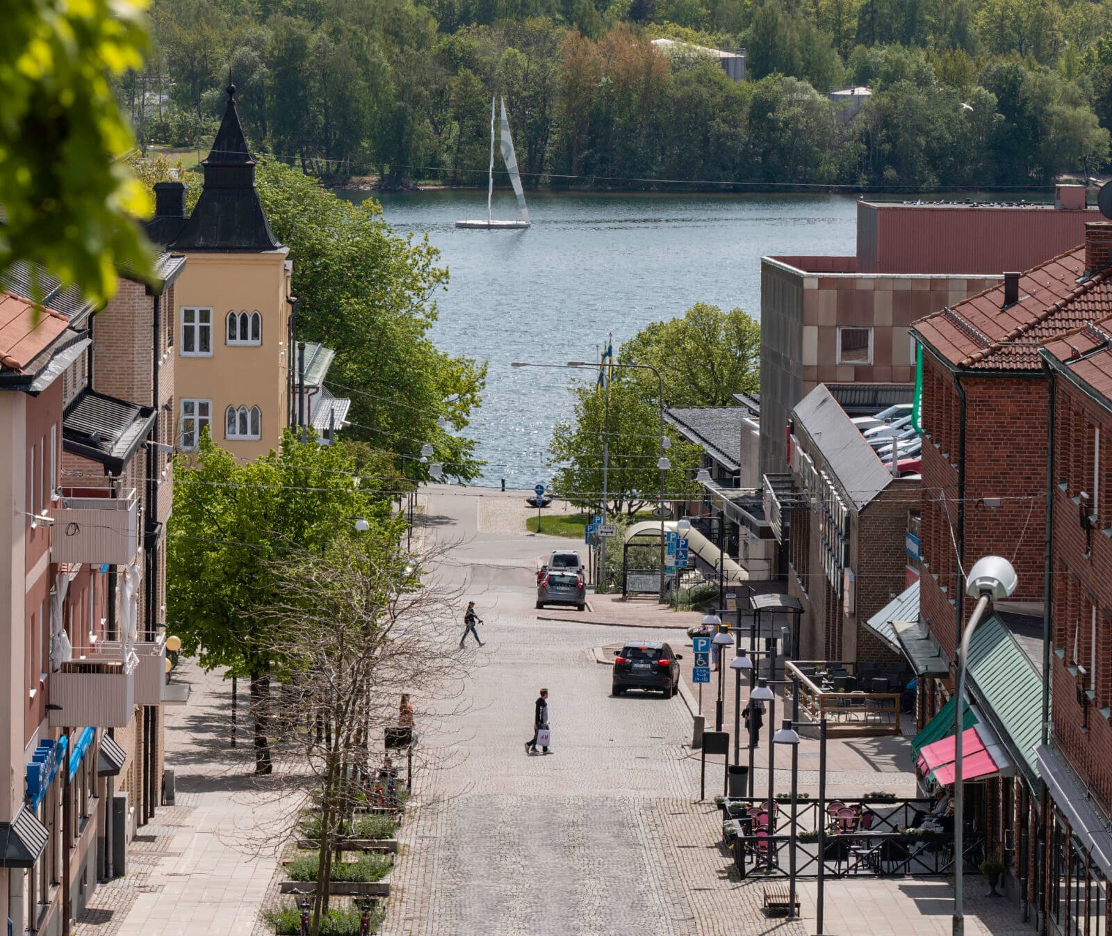 En gata med bilar i stan med landsbygdens skogsklädda berg i bakgrunden