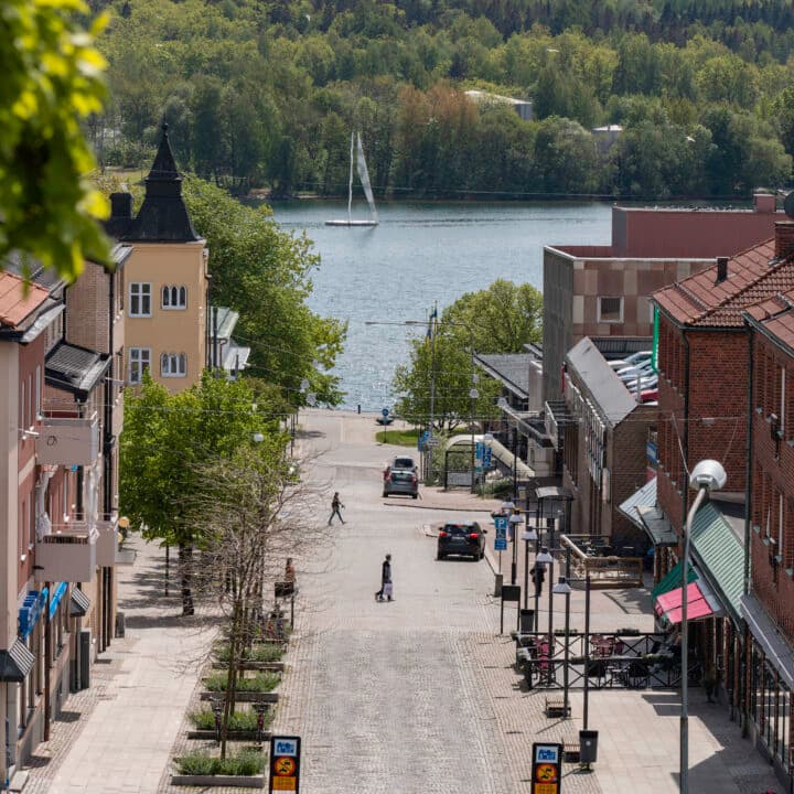 En gata med bilar i stan med landsbygdens skogsklädda berg i bakgrunden