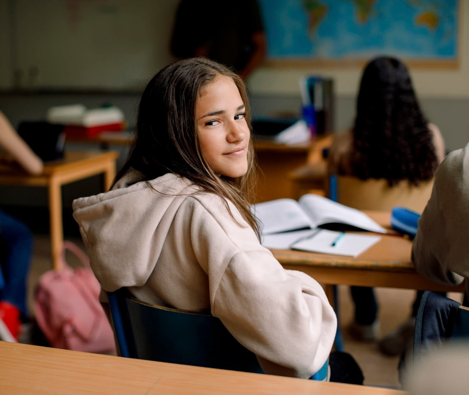 Bilden visar en klassrumsmiljö där en ung flicka sitter vid en skolbänk och tittar tillbaka mot ...