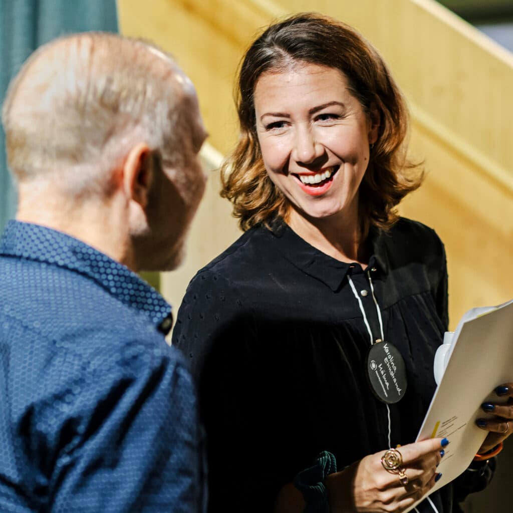 Bilden visar två personer som verkar vara i en konversation. Kvinnan till höger i bilden ler och ...