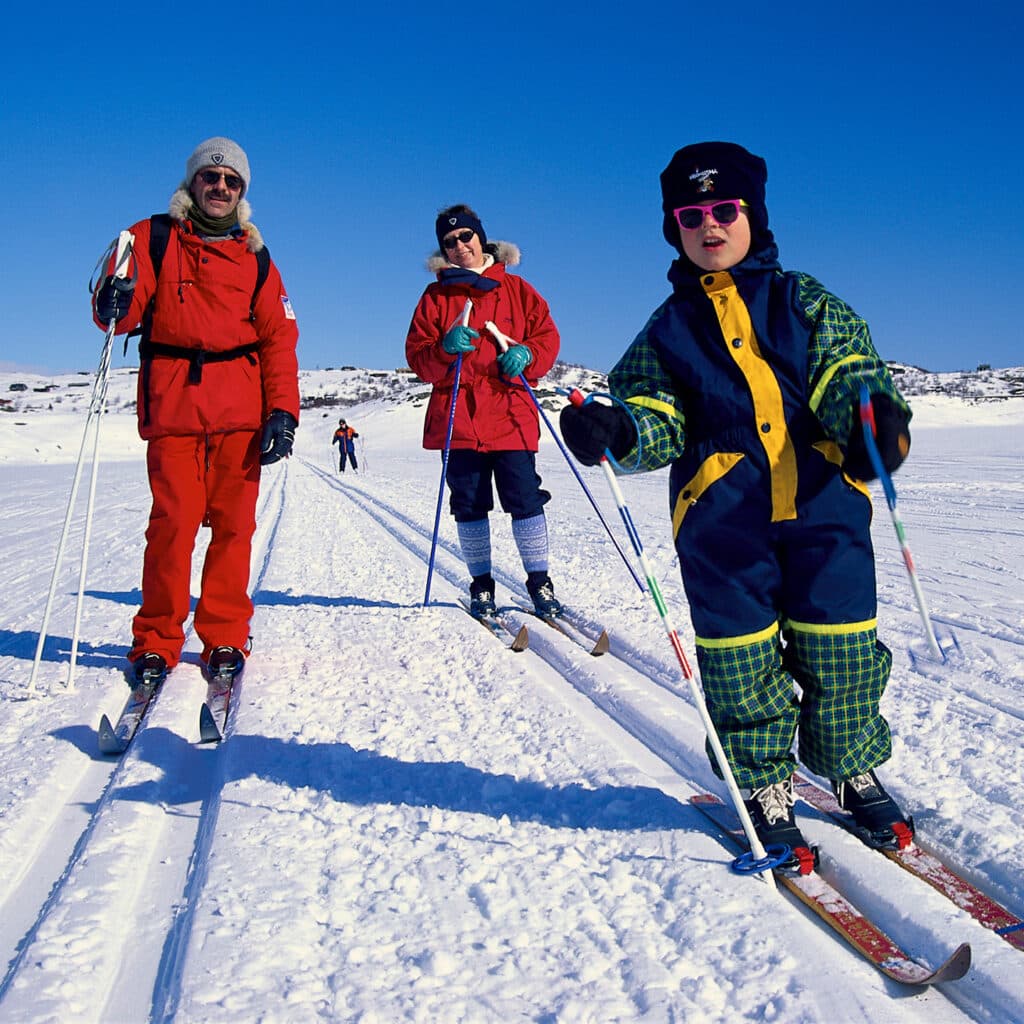 En familj åker skidor en solig vinterdag på sportlovet.